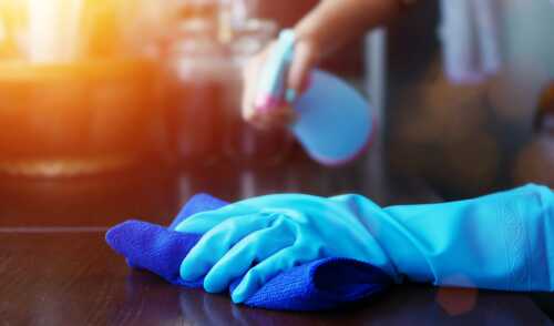 Nærbilde av en hånd med en lyseblå gummihanske og en blå klut. I den andre hånden holder person