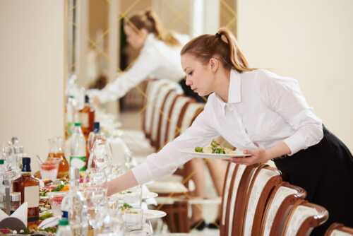 To kvinner ikledd hvit skjorte som dekker bordet fint og serverer mat
