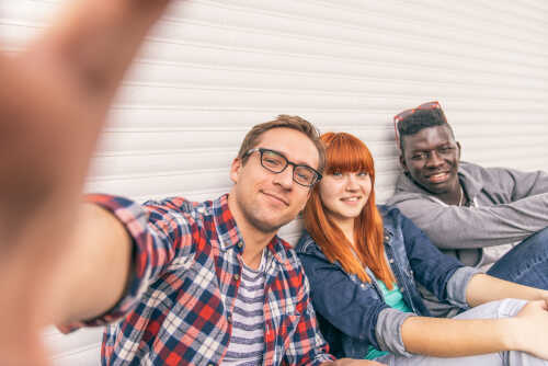 Tre studenter som sitter sammen, bildet er tatt som en selfie. De smiler til kamera