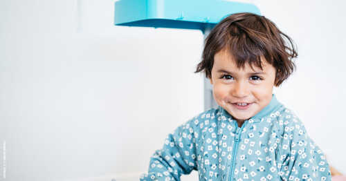 Barn ikledd blå jakke, smiler lurt til fotografen