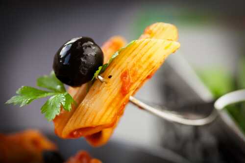 Pasta pens with tomato sauce and a black olive, on a fork