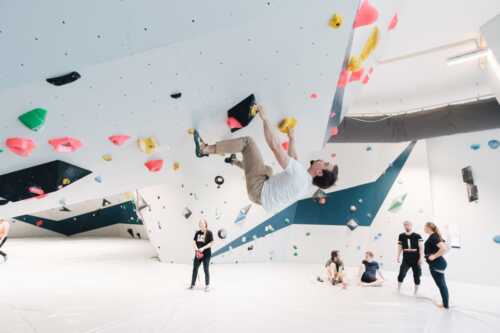 Picture from the climbing hall, a man climbs in one wall, there are several types of climbing walls.