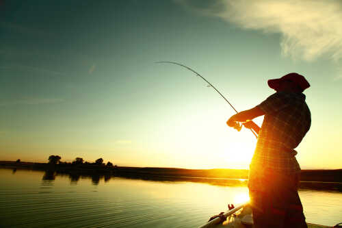 En person står å fisker med fiskestang, vi ser bare konturene av et menneske. Solnedgangen fyller 