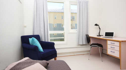Student hybel innredet med en seng, godstol og skrivepult 