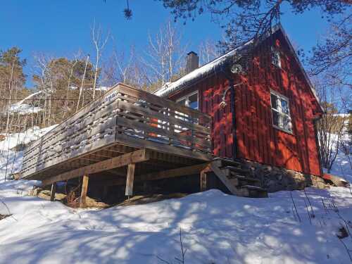 Picture of the student cabin seen from the outside, it is red with a terrace with yards around. Ther