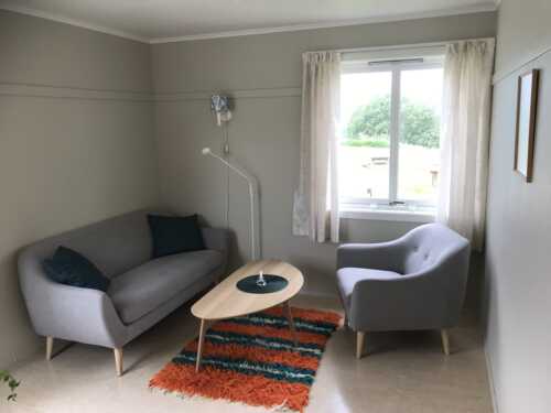 Trivelig stue som er innredet med to grå sofer, et lite bord og lyse gardiner