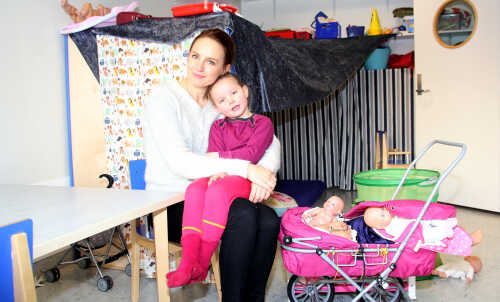Daughter sits on the lap of her mother, around them are a lots of toys