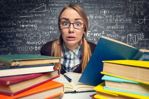 Stressed student surrounded by books, behind her is a blackboard with formulas and numbers