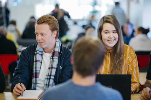 To mannlige og en kvinnelig student. Den kvinnelige studenten ser inni kamera med et nervøst smil.