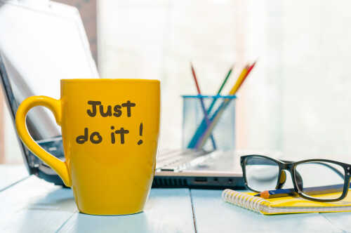 Bilde av en pult, hvor en gul kopp med teksten "Just do it!" er i fokus. Det står også en kopp med